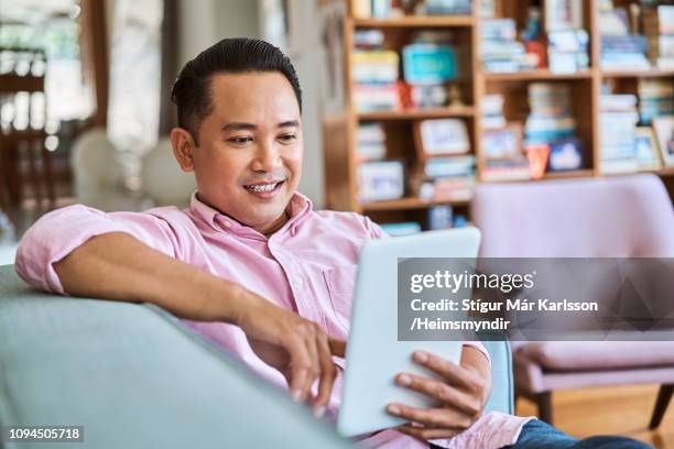 lächelnder mann mit digital-tablette im wohnzimmer - pink shirt stock-fotos und bilder