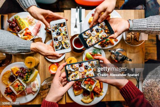 friends taking pictures of food on the table with smartphones during brunch in restaurant - photograph on table stock pictures, royalty-free photos & images