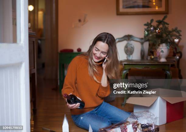 Woman unpacking Christmas parcel at home, talking on mobile phone