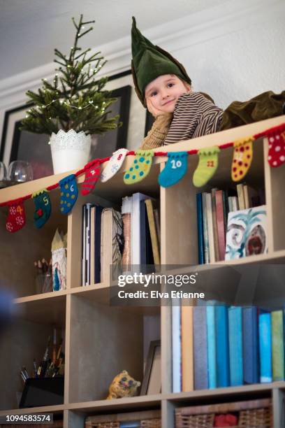child (6-7) dressed as an elf on top of a bookshelf - christmas countdown stock pictures, royalty-free photos & images