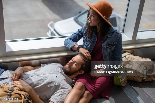 young mixed race woman looks out window as boyfriend rests in her lap while waiting at airport terminal gate. - airport hipster travel stockfoto's en -beelden