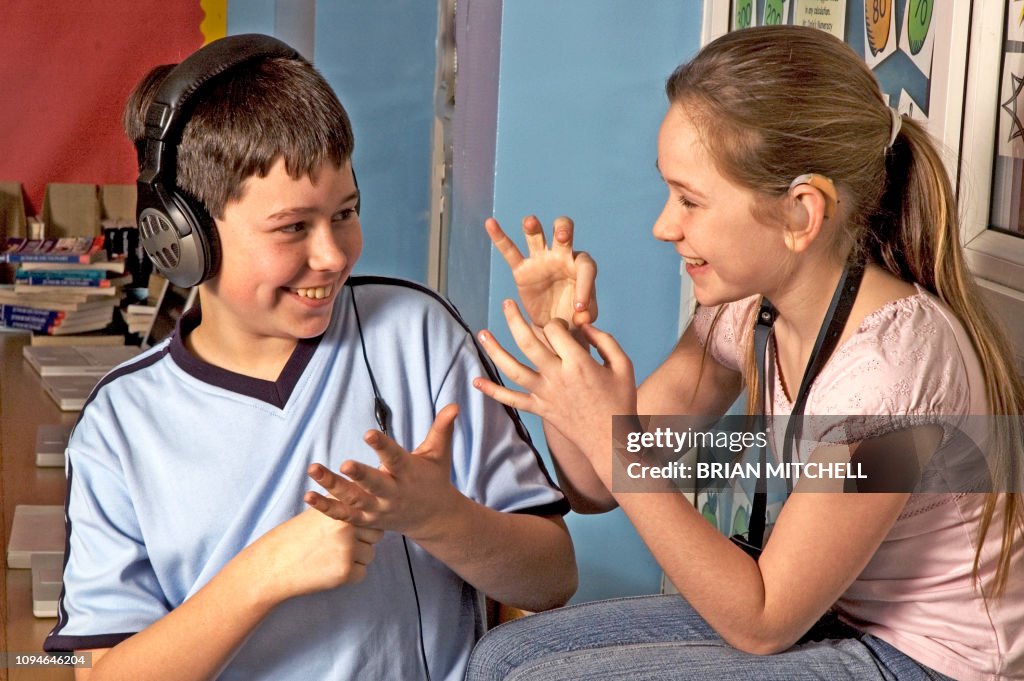 Deaf children with hearing aids in a school class room using sign language