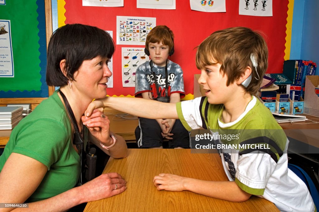 Deaf children with hearing aids in a school class room using sign language