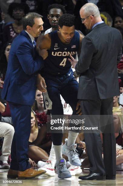 Connecticut men's basketball athletic trainer James Doran, left, and head coach Dan Hurley, right, help Connecticut guard Jalen Adams off of the...