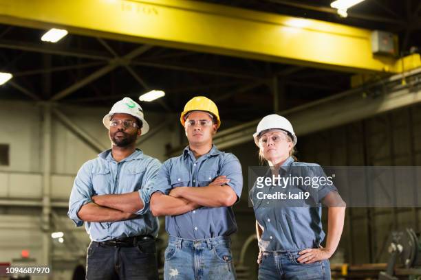 three workers with hardhats standing in warehouse - female with group of males stock pictures, royalty-free photos & images