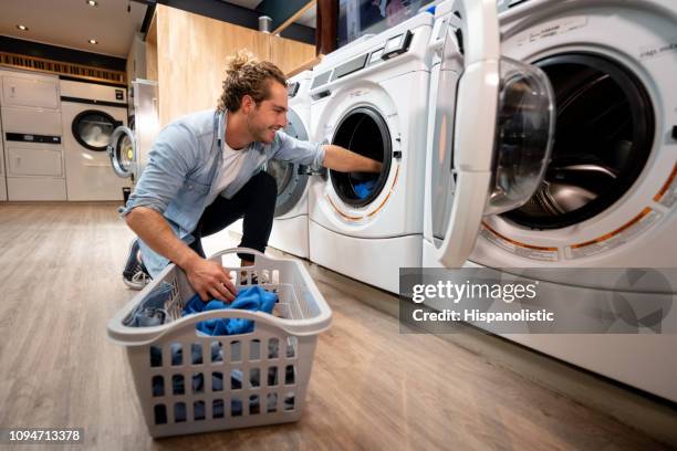 young customer at a self service laundry loading washing machine smiling - lavandaria imagens e fotografias de stock