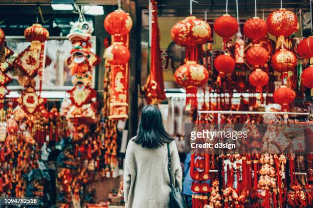 rear view of woman standing against various chinese new year decorations and ornaments on city street - prosperity stock pictures, royalty-free photos & images