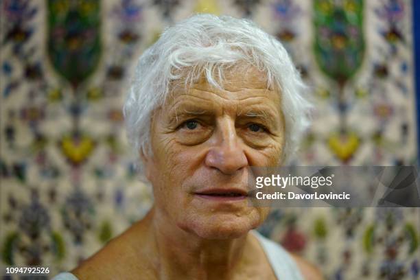 portrait of senior man with blurred bokhara carpets in background, bukhara, uzbekistan - uzbekistan market stock pictures, royalty-free photos & images
