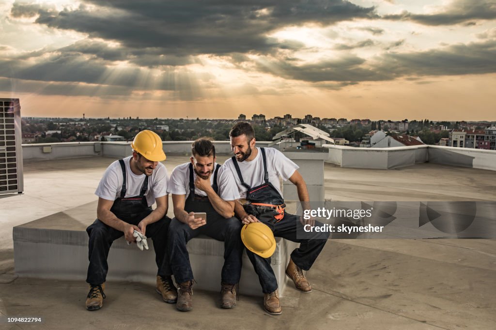 Glückliche Arbeiter mit Handy auf einem Dach nach der Arbeit.