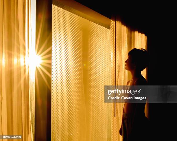 side view of thoughtful shirtless boy standing by window in darkroom at home - dark room foto e immagini stock