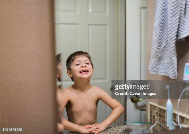 shirtless smiling boy with broken teeth looking in mirror while standing at home - losing virginity - fotografias e filmes do acervo