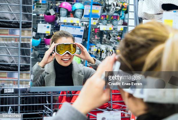 vrouw winkelen skibrille, controleren van zichzelf in een spiegel bij sport shop - sportswear shopping stockfoto's en -beelden