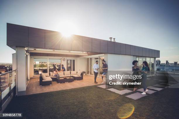 young happy friends talking while spending their time on a penthouse terrace. - penthouse stock pictures, royalty-free photos & images