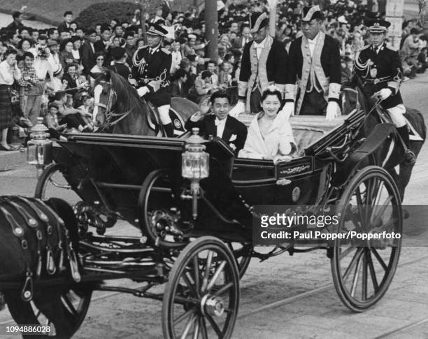 Crown Prince Akihito of Japan pictured on left with his wife Princess Michiko seated in a horse drawn carriage as they wave to cheering crowds of...