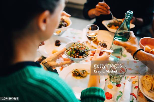 high angle view of woman serving salad from bowl while sitting by friend holding bottle at table in restaurant - brunch stock-fotos und bilder