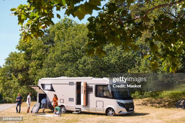 family unloading motor home parked against trees at trailer park - family caravan stock pictures, royalty-free photos & images