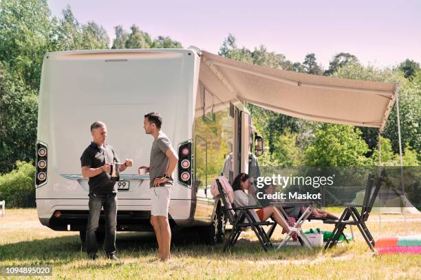 senior man talking to son while family relaxing outside van at campsite - family caravan stockfoto's en -beelden