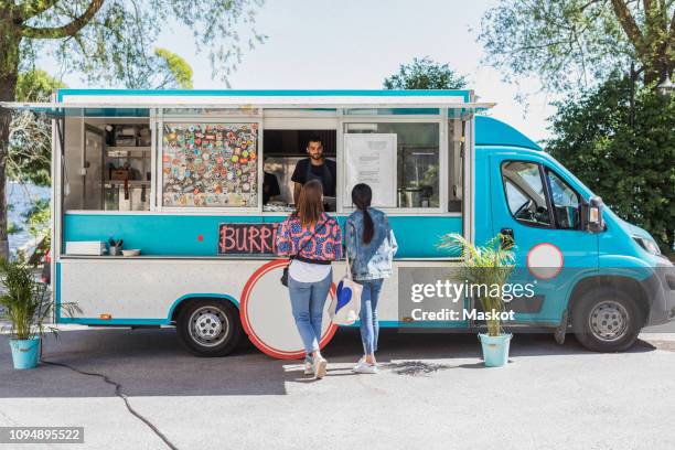 full length rear view of female friends talking with male food truck owner in city on sunny day - furgone ambulante foto e immagini stock
