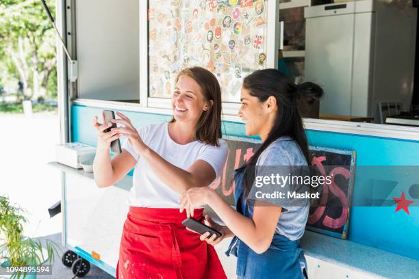 happy young multi-ethnic female owners using smart phone while standing at concession stand - imbissbude stock-fotos und bilder