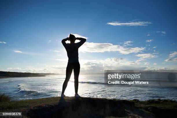 silhouette of sports woman with hands behind head looking out to sea. - stretching hands behind head rear view stock-fotos und bilder