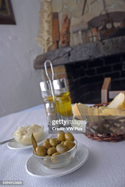 Table with alioli, spanish green olives, bread and oil, salt, pepper and vinegar, with a rural chimney behind, in an ibizan restaurant located on the...