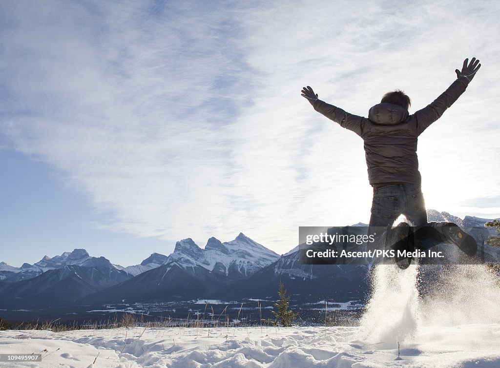 Man jumps for joy in snowy mountain meadow