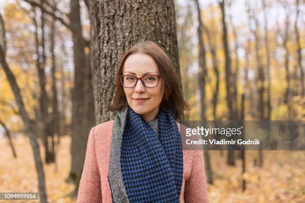 portrait confident woman in scarf standing against tree in autumn park - short trees bildbanksfoton och bilder