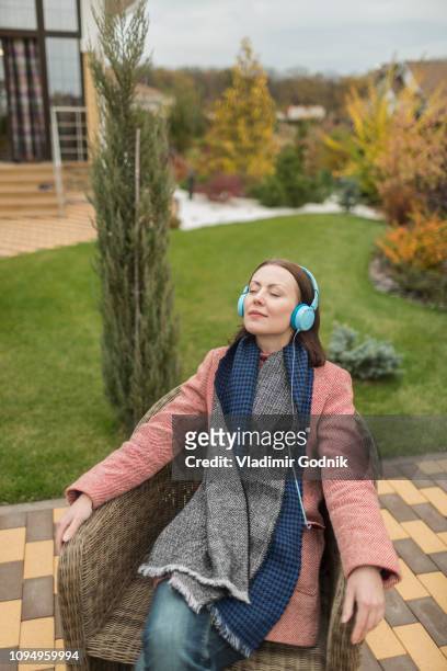 serene woman in scarf and coat listening to music with headphones on autumn patio - voronezh stock pictures, royalty-free photos & images