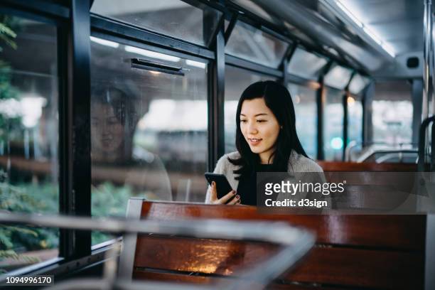 young woman looking at smartphone while riding tram in the city - hong kong mass transit fotografías e imágenes de stock