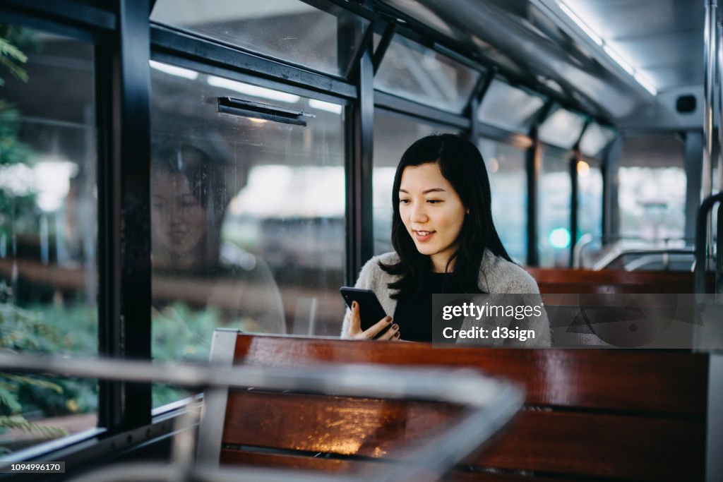 Young woman looking at smartphone while riding tram in the city