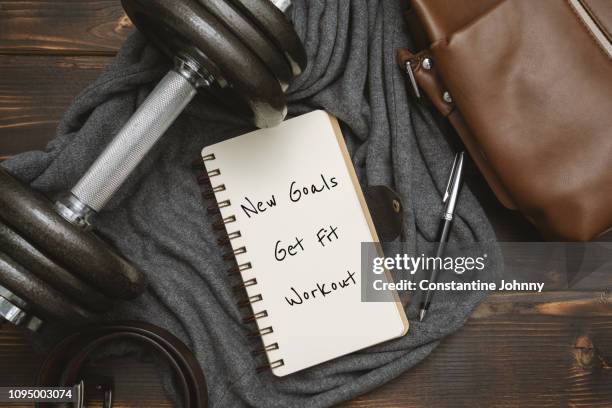 new year's goals and resolution written on notepad, with dumbbell and satchel man's bag on rustic wood - exercise equipment stock pictures, royalty-free photos & images