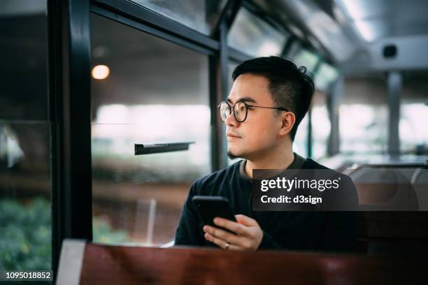 smart young man using smartphone while riding tram in the city - commuter bus stock pictures, royalty-free photos & images