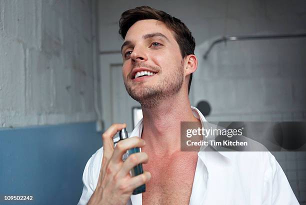 man putting on cologne in urban loft bathroom - parfum stock-fotos und bilder