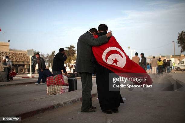 Two men, one wearing the flag of Tunisia, stand at the border of Libya on February 28, 2011 in Ras Jdir, Tunisia. As fighting continues in and around...