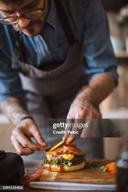 köstliche cheeseburger hinzufügen letzte details - hipster in a kitchen stock-fotos und bilder