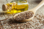 Heap of Flax seeds or linseeds in spoon and bowl with glass of linseed oil on wooden backdrop. Flaxseed or linseed concept. Flax seed dietary fiber
