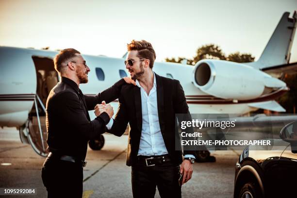 rich colleagues doing the bro shake on an airport runway next to a private airplane - billionaire stock pictures, royalty-free photos & images
