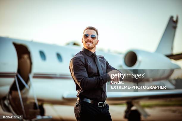 rich and successful young businessman looking at his watch in front of a private airplane - status symbol stock pictures, royalty-free photos & images