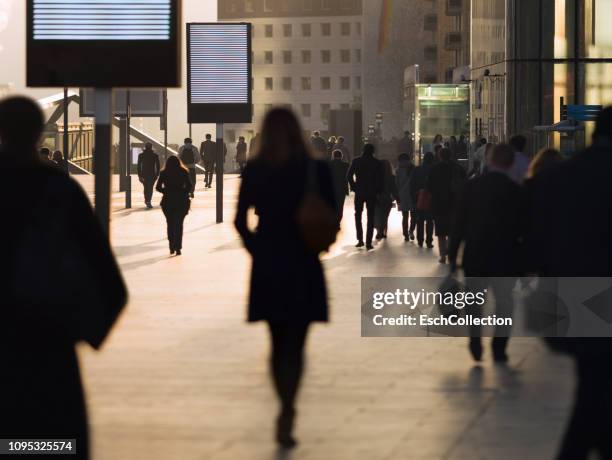 silhouette of businesswoman among other commuters at modern business district - crowd chasing stock pictures, royalty-free photos & images