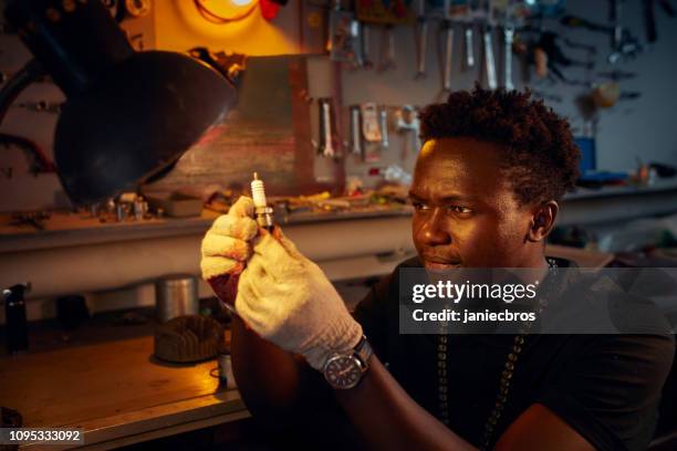 african ethnicity man in workshop checking on motorcycle spark plug - spark plug stock pictures, royalty-free photos & images