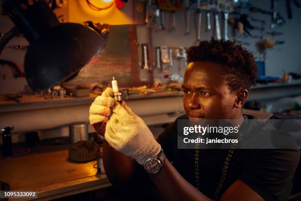 african ethnicity man in workshop checking on motorcycle spark plug - motorcycle workshop stock pictures, royalty-free photos & images