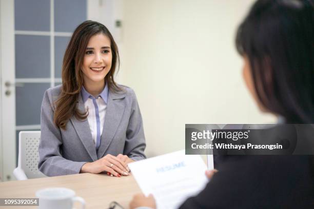 smiling businesswoman holding resume and talking to female candidate during corporate meeting or job interview - curriculum vitae fotografías e imágenes de stock