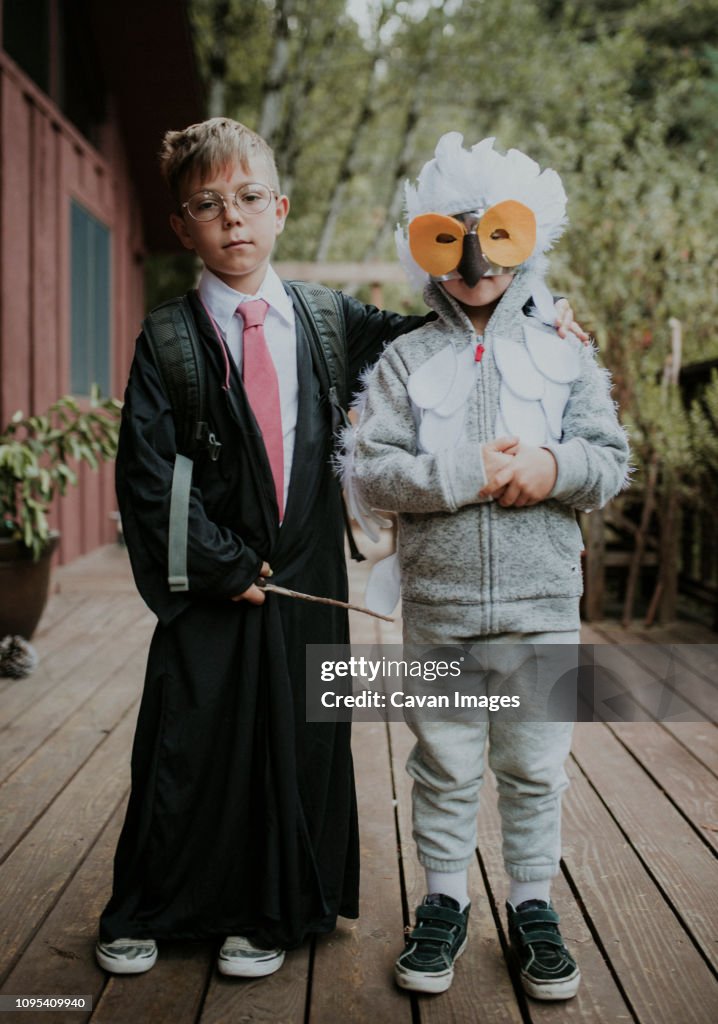 Full length portrait of brothers dressed up as Harry Potter and owl on floorboard during Halloween
