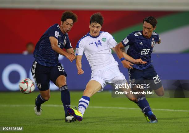 Eldor Shomurodov of Uzbekistan beats Genta Miura and Tomoaki Makino of Japan as he scores his team's first goal during the AFC Asian Cup Group F...