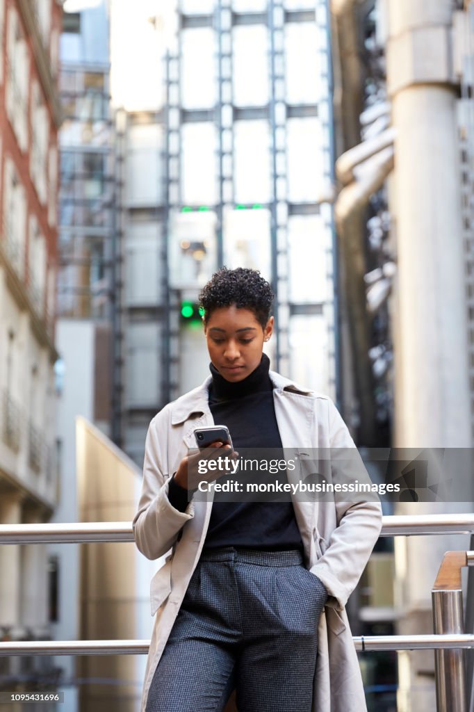 Modisch junge schwarze Frau in der Stadt stützte sich auf ein Handlauf mit ihrem Smartphone, vertikale
