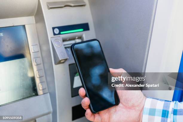 man checking his smartphone screen near atm machine - online bank statement stock pictures, royalty-free photos & images