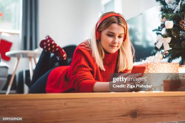 girl lying on the floor next to the christmas tree listening to music - santa hat stock pictures, royalty-free photos & images