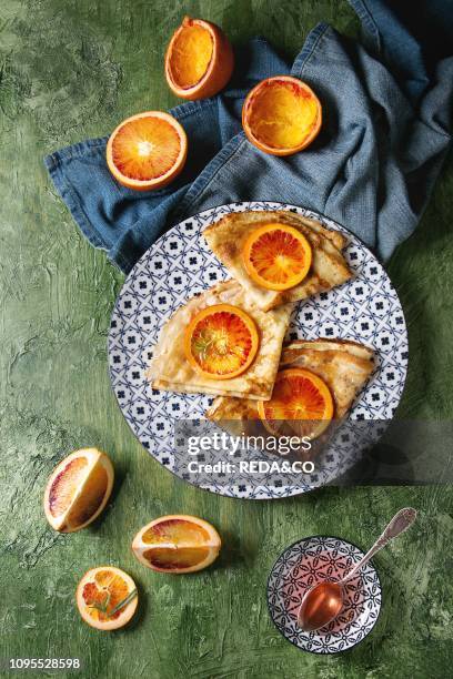 Homemade crepes pancakes served in white decorate ceramic plate with bloody oranges and rosemary syrup with sliced sicilian red oranges and blue...