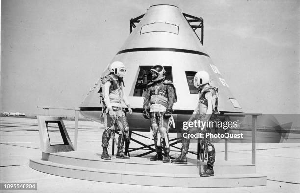 Portrait of three unidentified astronauts in NASA flight suits as they pose beside a mock-up of a proposed Apollo capsule design, Cape Canaveral,...