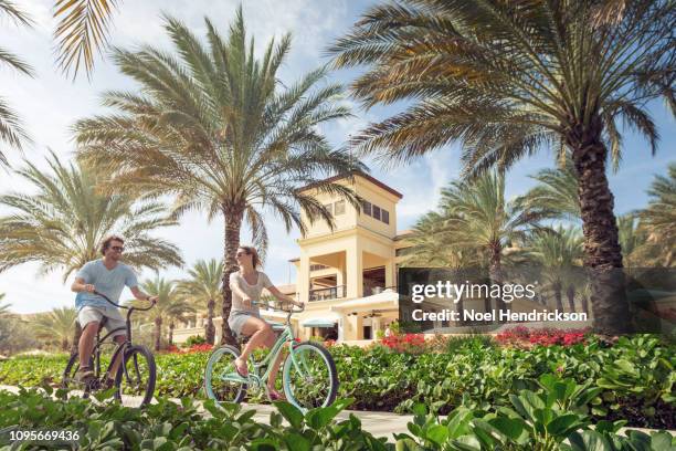 couple riding bicycles through a palm-lined luxury resort - willemstad stockfoto's en -beelden